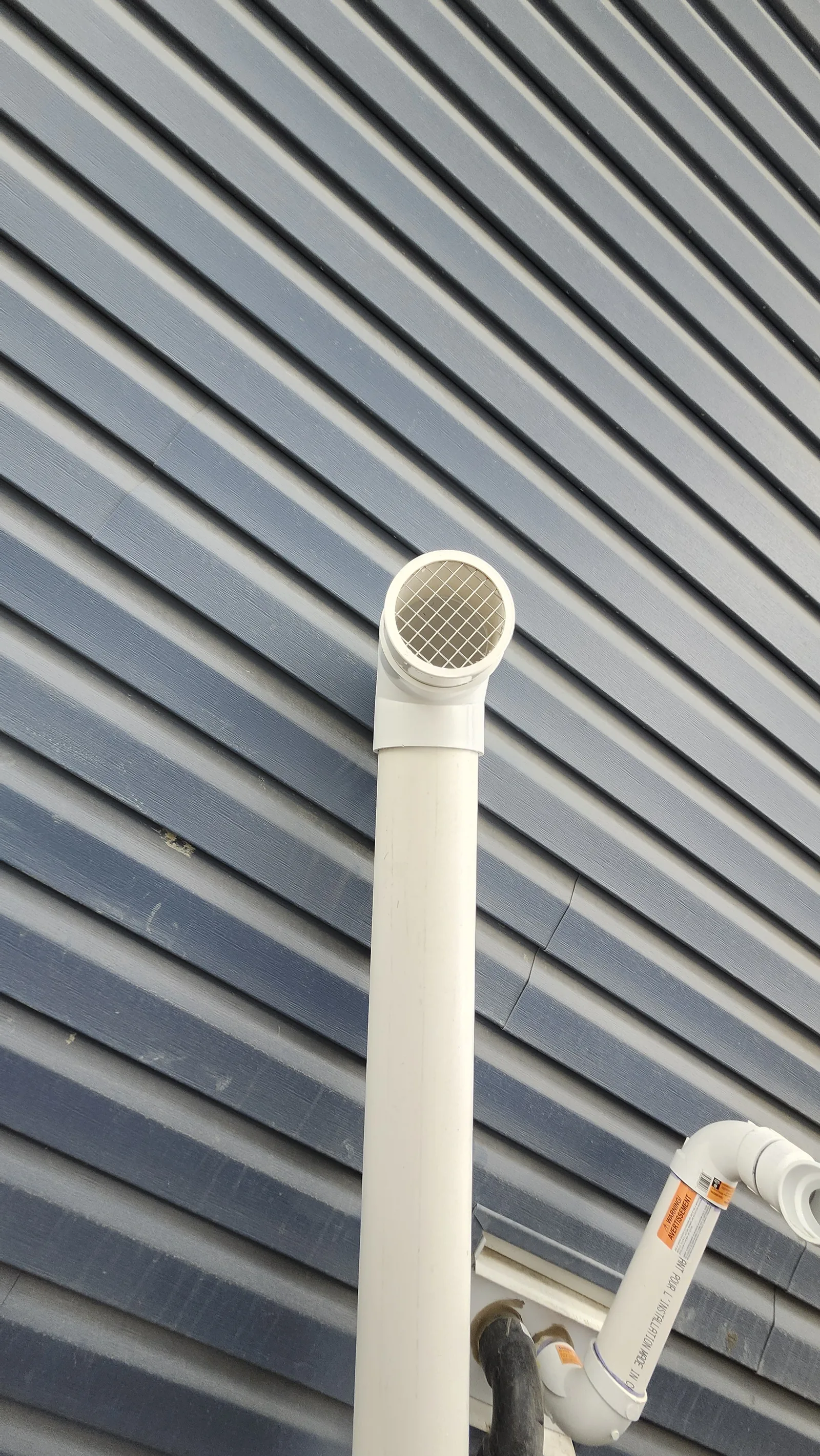 Radon Discharge Pipe With A Screened Outlet On Blue Vinyl Siding Of A Cochrane Walkout