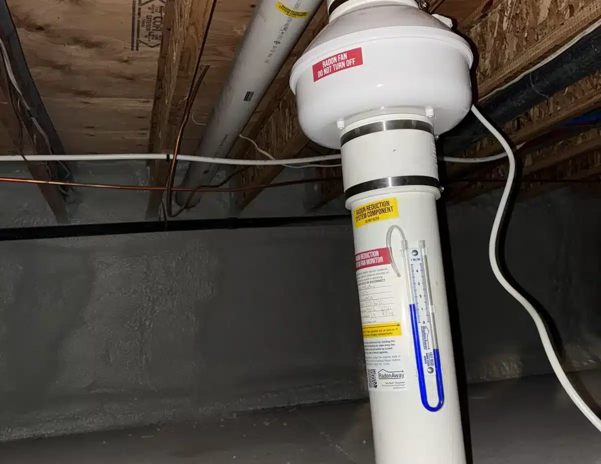 Radon Fan And Pressure Gauge On A Pipe In A Duplex Crawlspace With A Concrete Floor And Spray-Foamed Walls