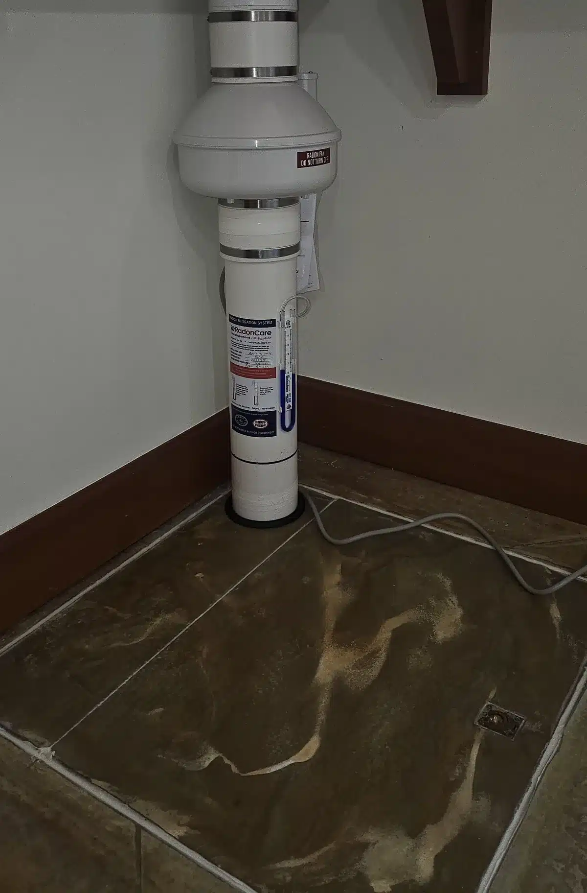 A Radon Fan In The Corner Of A Finished Basement Room Above A Sealed Sump Lid In A Sherwood Park-Area Home