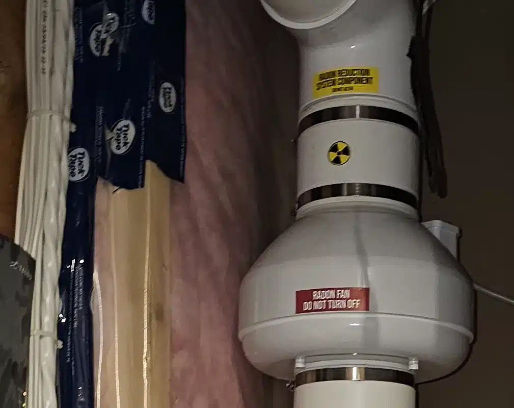 A Radon Fan With Warning Labels On The Pipe In A Basement Mechanical Room In Southwest Edmonton