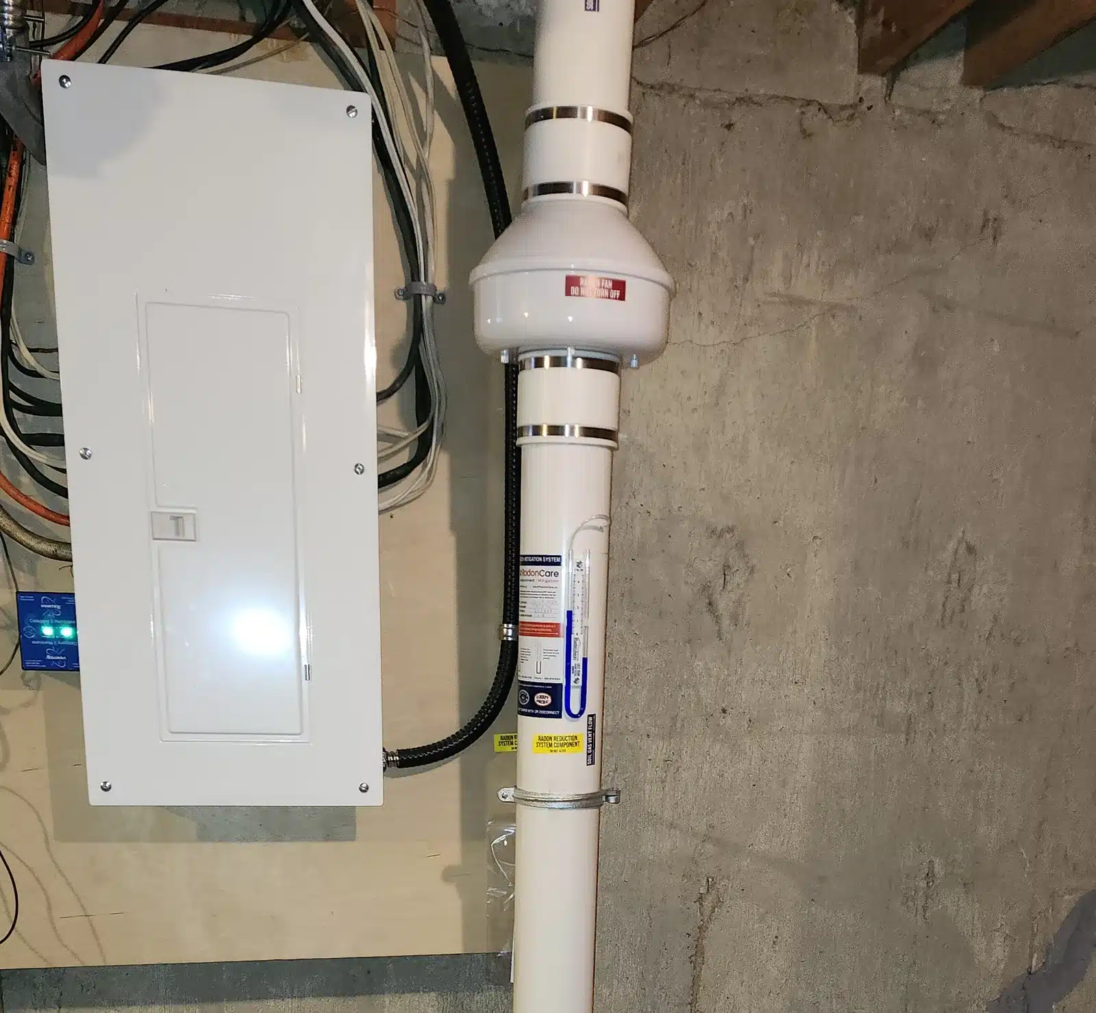 A Radon Fan And Labelled Pipe Beside The Electrical Panel In A Devon Basement
