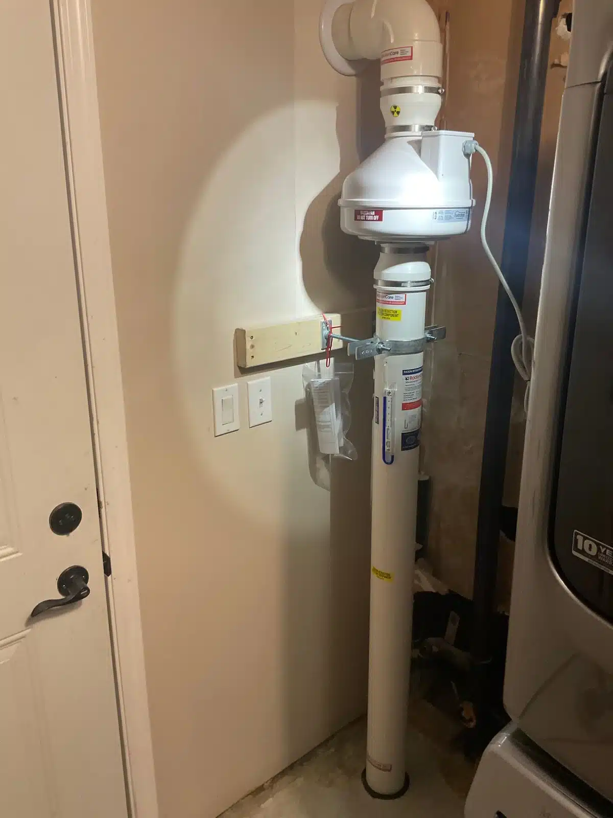 Radon Fan And Vent Pipe Beside A Laundry Room Door In Salmon Arm